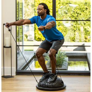 Strength Training Equipment- (300*300)- Man with gym outfit exercising with Black Bosu Ball and resistance band in an indoor setting with panoramic windows with a small pond and tall hedge visible outside