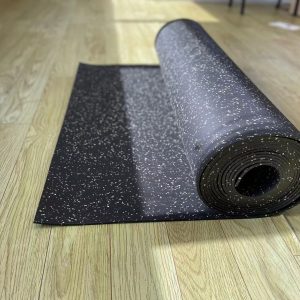 Gym Accessories- (300*300)- Side view of a Partially unrolled Black Flooring Mat (7000MM*1000MM*5MM) with multi-colour particles visible, on a wooden floor