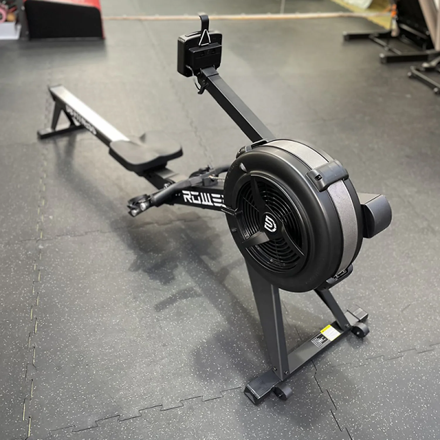 DB Fitness air rower three-quarter view highlighting the flywheel housing, rail, seat and monitor
