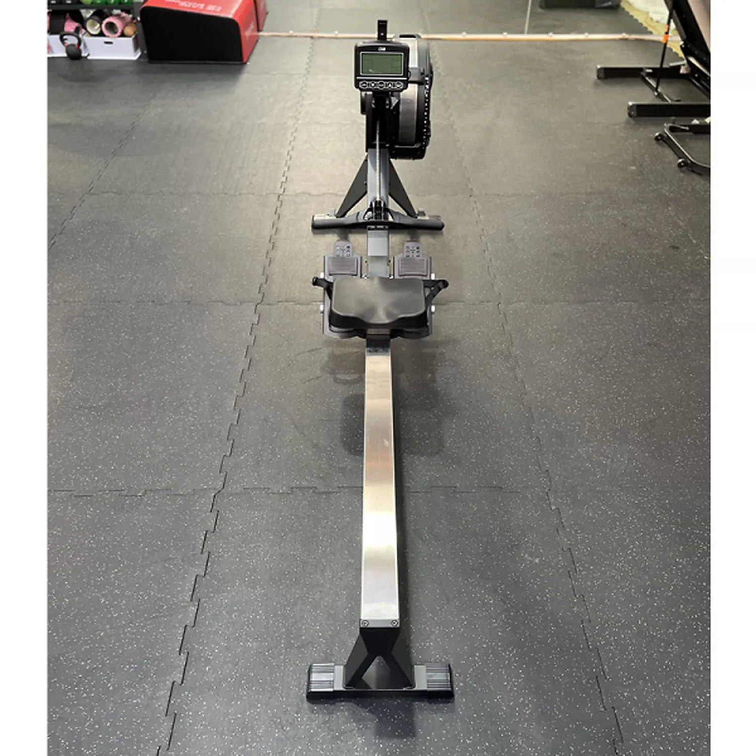 DB Fitness air rower full-length front view showing the rail, seat, footrests and performance monitor in a gym